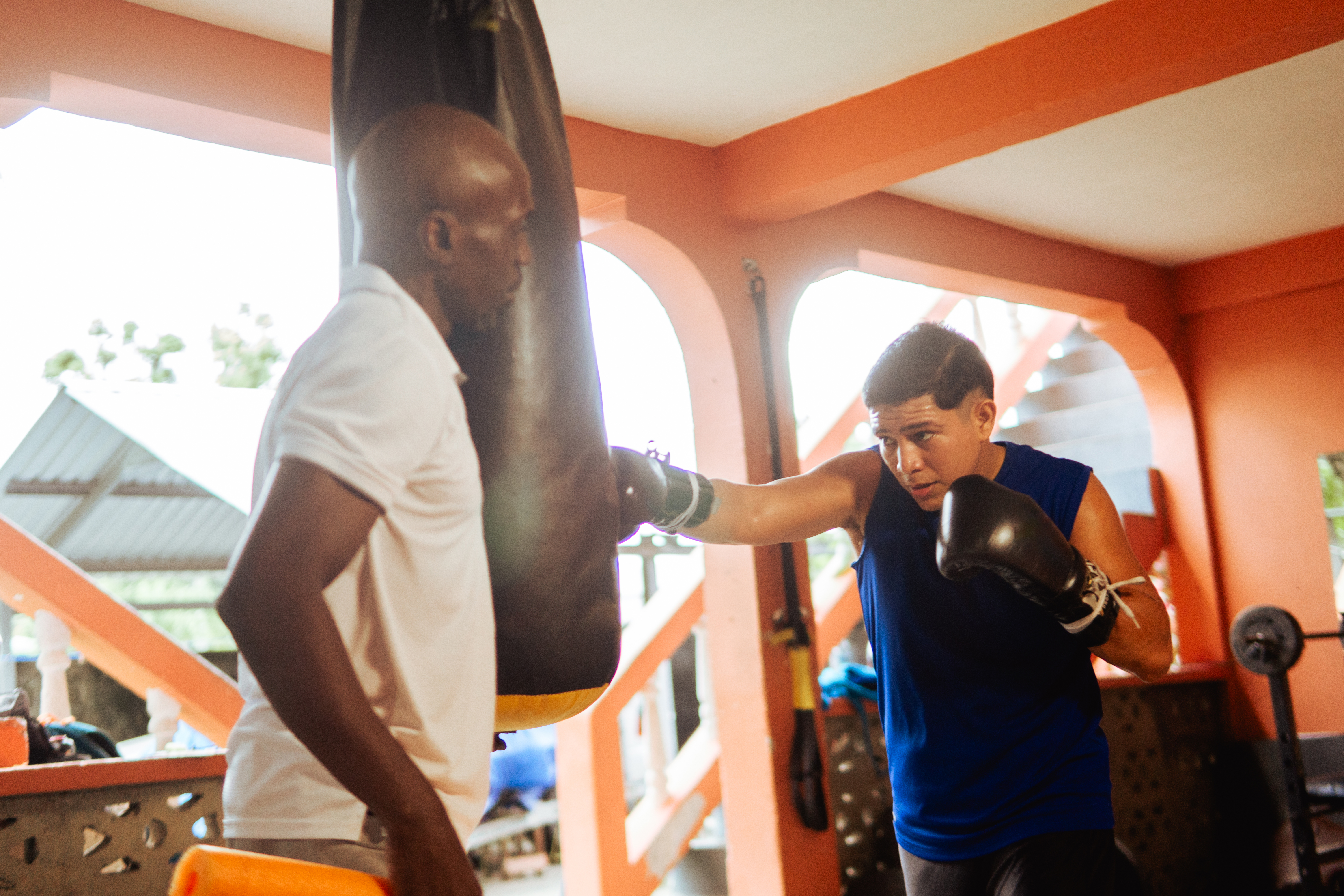 Hispanic man training with a punching bag while coach observes in a home gym